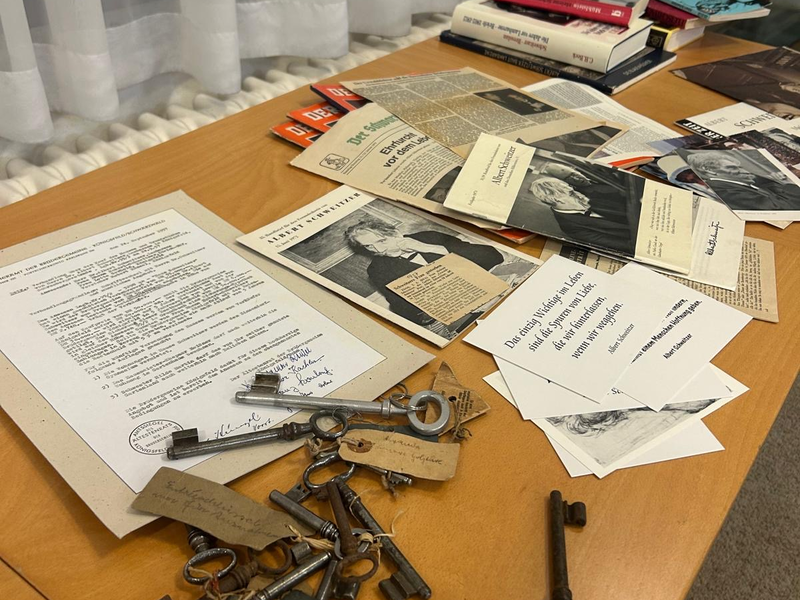 Ein Tisch mit Dokumenten, alten Schlüsseln und mehreren Büchern unter einem Fenster mit Vorhängen.