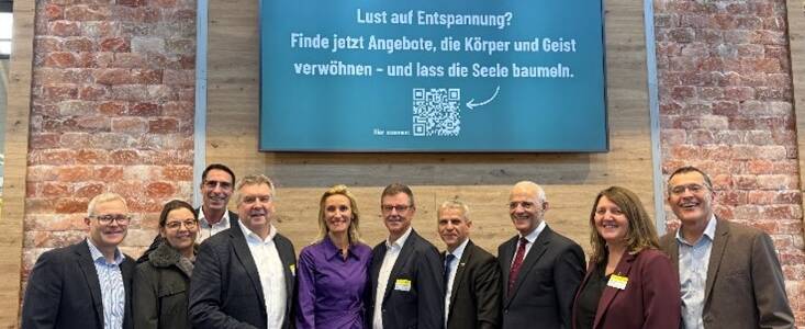 Eine Gruppe von zehn Personen steht vor einer Wand mit einem Schild, das zur Entspannung einlädt und einen QR-Code zeigt.
