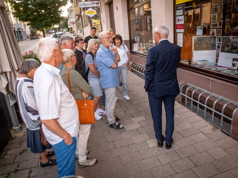 Eine Gruppe von Menschen steht vor einem Schaufenster und hört einer Person zu, die drinnen zu ihnen spricht.