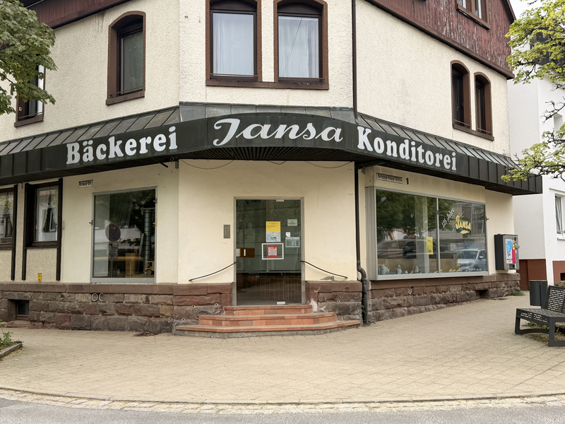 Das Bild zeigt die Front einer Eckbäckerei und Konditorei mit dem Namen "Jansa", die eine einladende Eingangstür und große Schaufenster hat.