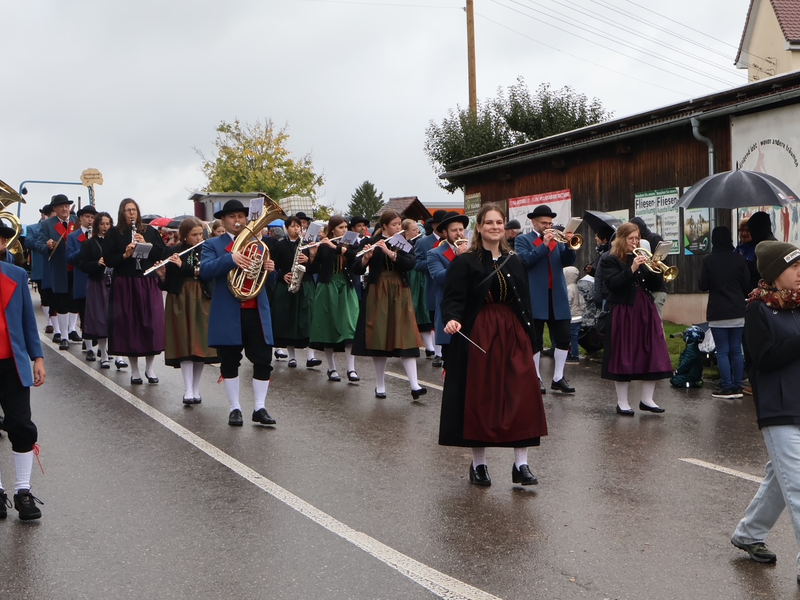 Eine Blaskapelle marschiert in traditioneller Tracht bei einem Umzug eine Straße entlang.