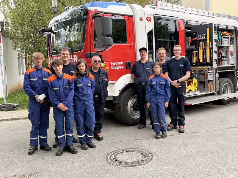 Eine Gruppe von Feuerwehrleuten in blauer Schutzkleidung steht vor einem Feuerwehrauto.
