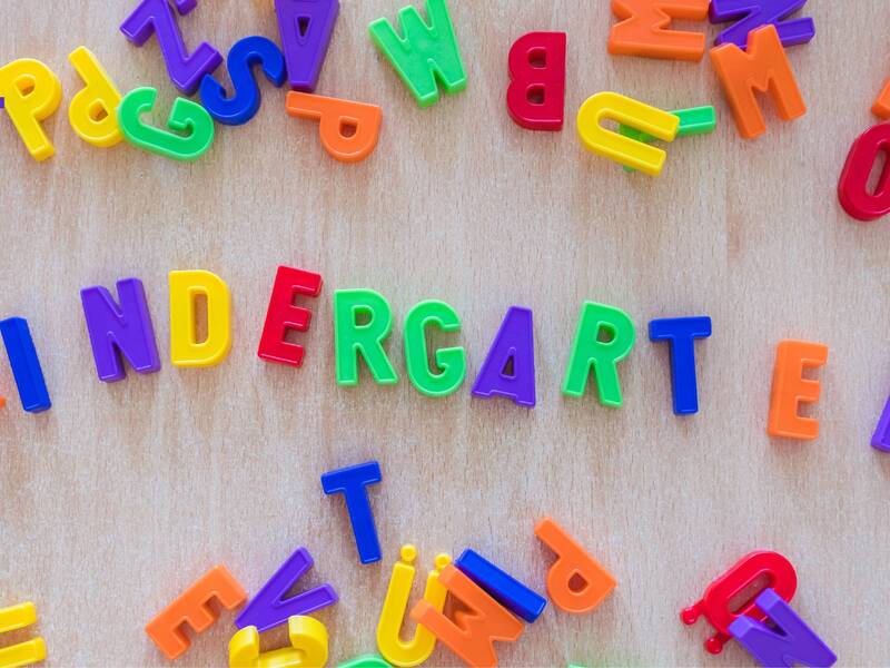 Bunte magnetische Buchstaben auf einer Holzoberfläche bilden das Wort "KINDERGARTEN".