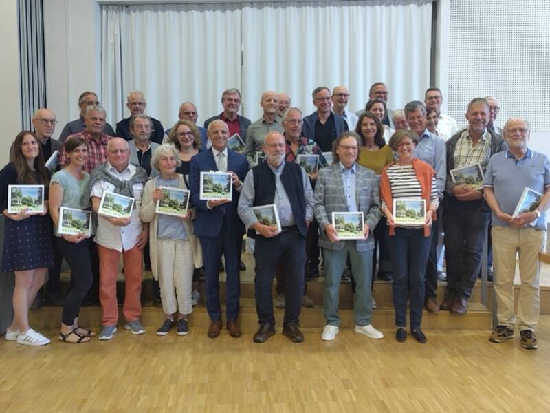 Eine große Gruppe von Menschen posiert in einem Raum, einige halten Bücher in der Hand.