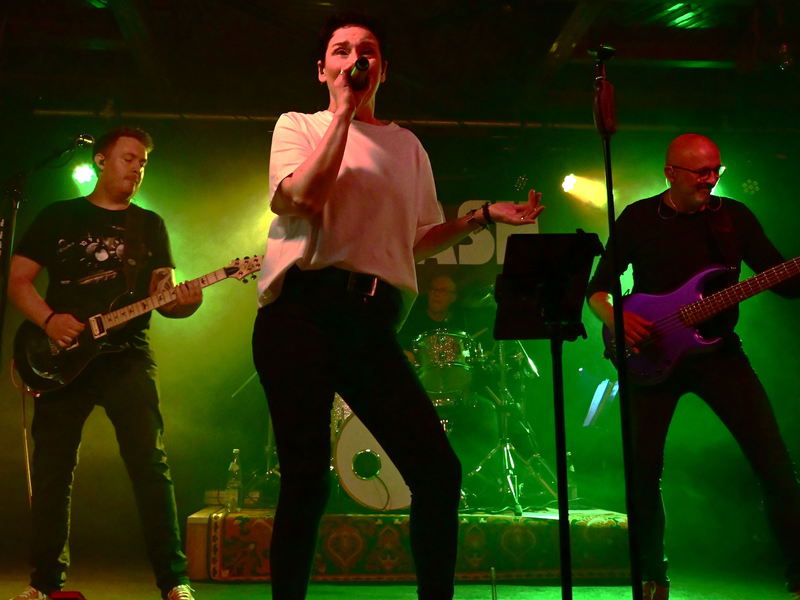 Vierköpfige Band mit Sängerin und zwei Gitarristen spielt auf einer Bühne in stimmungsvollem Licht.